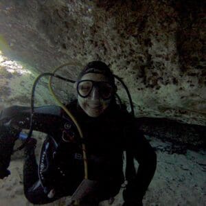 A man in black wetsuit and goggles sitting on ground.