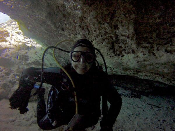 A man in black wetsuit and goggles sitting on ground.