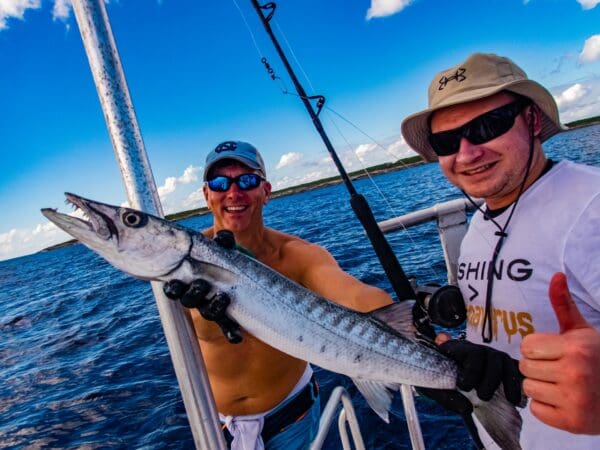 Two men holding a fish on the side of a boat.