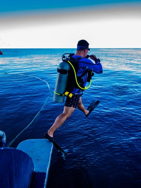 A man in blue shirt and shorts jumping off boat.