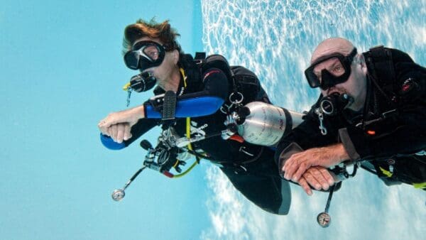 A woman in black wetsuit and goggles diving.