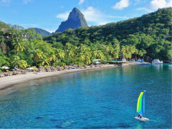 A sailboat is sailing in the ocean near a beach.