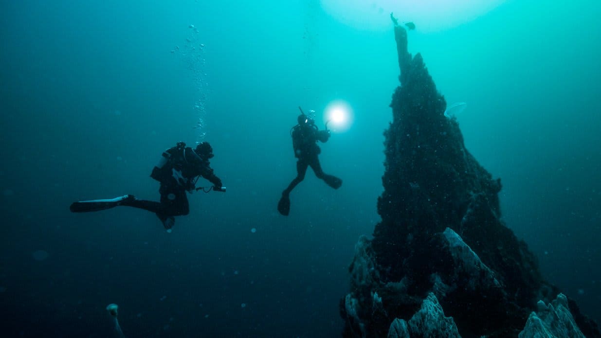 Two divers explore an underwater rock formation.