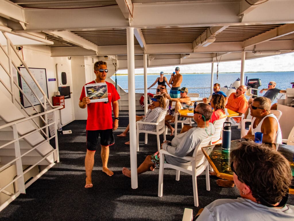 A man holding up an ipad while standing on the deck of a boat.