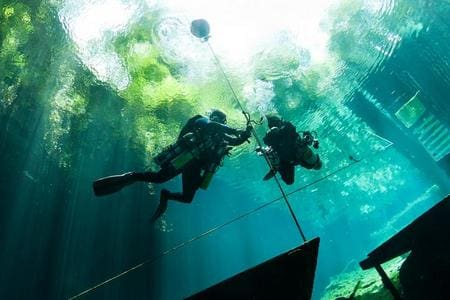 Two scuba divers are hanging from a rope.