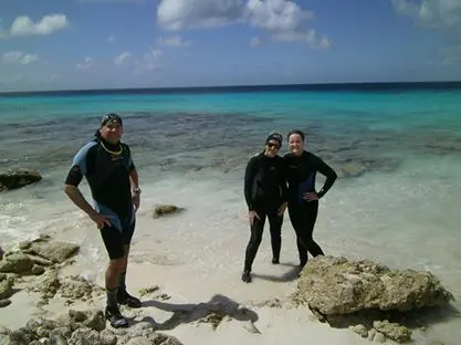 Three people in wetsuits on a beach.