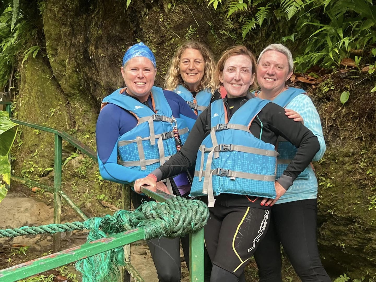 Four women in life jackets by a jungle.